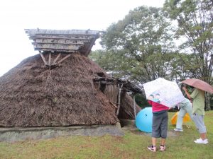 竪穴住居の復元に入ってゆく雨の中の二人の児童。